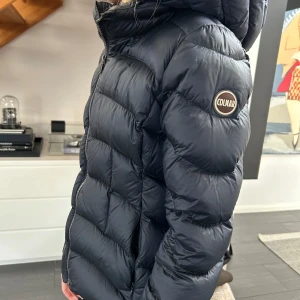 Svart dunjacka från Colmar - Säljer en stilren svart dunjacka från Colmar. Jackan har en dragkedja framtill och en huva för extra värme. Perfekt för kyliga dagar. 