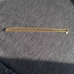 Guldfärgat halsband - Säljer ett stilrent guldfärgat halsband med en klassisk kedjedesign. Perfekt för att lägga till en touch av elegans till din outfit. Halsbandet har en enkel låsning och en glänsande finish. Kedjan är jag ord av råstfritt stål med en guldplättering över i 18 karat guld. Kedjans dimensioner är 50 cm lång och 5 mm bred.