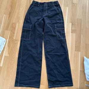 Svarta cargobyxor från Hollister - Snygga svarta cargobyxor från Hollister med vita sömmar och praktiska fickor på sidorna. Byxorna har en hög midja.