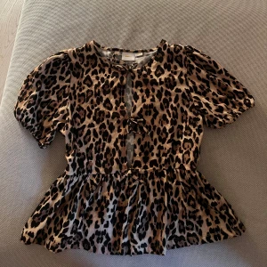 Leopardmönstrad blus med volang - Trendig leopardmönstrad blus med korta ärmar och volangdetalj i nederkant.