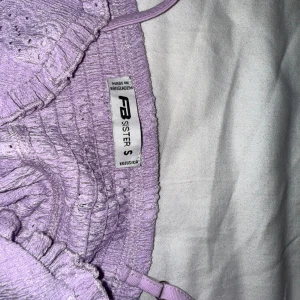 Lila ribbad topp från FB Sister - Säljer en söt lila ribbad topp från FB Sister. Toppen har smala axelband och en volangdetalj framtill. Perfekt för varma dagar eller som ett lager under en jacka.