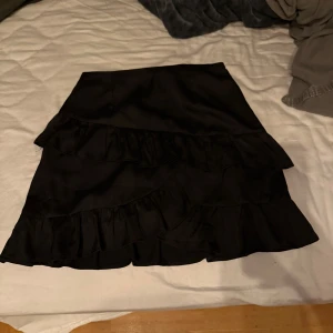 Svart kjol med volanger från Bik Bok - Snygg svart kjol från Bik Bok med flera lager av volanger. Har även en dragkedja på sidan.