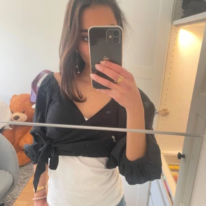 Svart omlottopp med knyt - Snygg svart omlottopp med knyt i midjan och långa ärmar. Perfekt för en stilren look. Passar bra över en vit topp