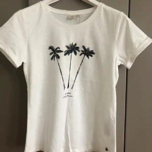 Vit t-shirt med palmmotiv från Cream - Säljer en vit t-shirt från Cream med ett coolt palmmotiv på framsidan. T-shirten har en rund hals och korta ärmar, perfekt för en avslappnad stil. Tillverkad i mjuk bomull för extra komfort.