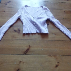 Rosa-lila ribbad tröja - Säljer en söt rosa-lila  ribbad tröja med v-ringning och knappar framtill. Den är croppad och har långa ärmar, perfekt för lager på lager-stil. Passar bra till både jeans och kjol. 🌸