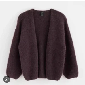 Mörklila teddyjacka - Säljer en mysig vinröd kofta med långärmad design. Koftan har en öppen front och en loose passform, perfekt för kyliga dagar. Den är tillverkad i ett mjukt och fluffigt material som ger en avslappnad look.