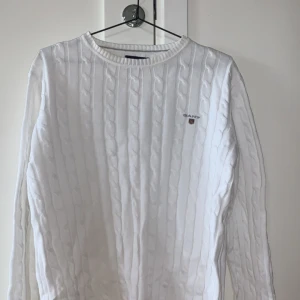 Vit kabelstickad tröja från GANT - Säljer en stilren vit kabelstickad tröja från GANT. Tröjan har en klassisk rund halsringning och långa ärmar. Perfekt för en elegant och avslappnad look. Tröjan är i mycket bra skick och säljs på grund av att jag har vuxit ur den. Hör gärna av er kring funderingar!!