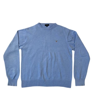 Ljusblå tröja från GANT - Säljer en stilren ljusblå tröja från GANT med broderad logotyp på bröstet. Tröjan har en rund halsringning och ribbade muddar vid ärmslut och nederkant. Perfekt för en avslappnad och snygg look.