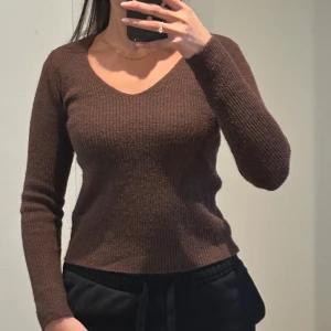 Brun  tröja - Säljer en snygg brun tröja med v-ringning. Tröjan har långa ärmar och en tight passform som framhäver figuren. Perfekt för en stilren look.
