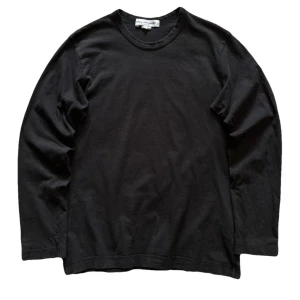 Svart långärmad tröja från Comme des Garçons - Säljer en stilren svart långärmad tröja från Comme des Garçons. Perfekt för en minimalistisk look. Tröjan är gjord i mjukt bomullsmaterial och har en klassisk rund halsringning. Passar till många olika outfits!