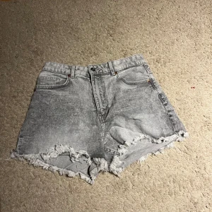 Grå jeansshorts från Divided H&M - Snygga grå jeansshorts från Divided, H&M med fransiga kanter och en cool tvättad look. Perfekta för en avslappnad stil. De har en klassisk femficksdesign och knappgylf. Skriv om det är något ni undrar!