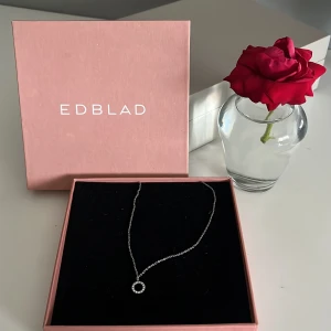 Silverhalsband med cirkel från Edblad - Stilrent halsband från Edblad i silverfärg med en tunn kedja och en rund cirkelberlock dekorerad med gnistrande stenar. Perfekt för dig som gillar minimalistiska smycken med en touch av elegans. Levereras i original ask.