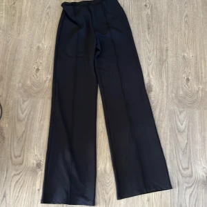 Svarta vida kostymbyxor Gina Tricot - Svarta kostymbyxor från Gina Tricot i storlek S. Byxorna har en hög midja och ett snyggt wide fit-snitt med raka, vida ben. Perfekta för en clean och stilren look. Materialet känns mjukt och följsamt.