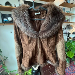 Brun pälsjacka med dragkedja - Säljer en brun pälsjacka med stor fluffig fuskpälskrage och detaljer i olika bruna nyanser. Jackan har dragkedja framtill, långärmade ärmar och inslag av stickat tyg på ärmarna. 