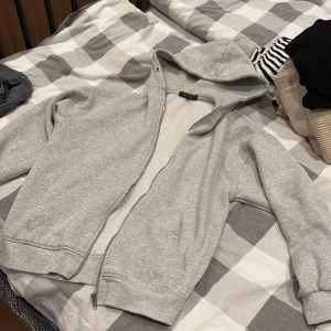 Grå hoodie från Missguided - Säljer en klassisk grå hoodie från Missguided i storlek 36. Tröjan har dragkedja framtill, huva och långa ärmar. Perfekt för chill dagar eller när du vill ha en enkel och stilren look. Tillverkad i mjuk bomullsblandning för extra komfort.
