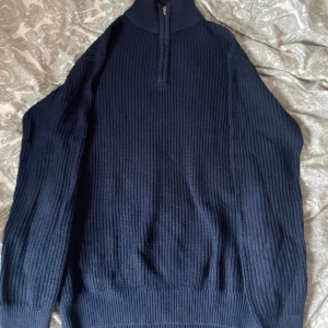 Mörkblå stickad half zip tröja - Mysig mörkblå stickad tröja med half zip och hög krage. Tröjan har ribbad struktur och långa ärmar, perfekt för kyliga dagar. Enkel, trendig och stilren design som passar till det mesta.