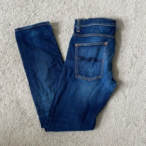 Blå jeans från Nudie Jeans  - Snygga blå jeans från Nudie Jeans Co med klassisk femficksdesign och kontrastsömmar. Jeansen har en rak passform och är tillverkade i slitstarkt denim med coola slitningar och detaljer på bakfickan.