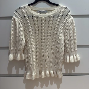 Vit stickad tröja med volang från Zara - Supersöt ljusbeige stickad tröja från Zara med volangdetaljer vid ärmslut och nederkant. Tröjan har ett hålmönster och rund halsringning. Använd några gånger men fortfarande bra skick 💞