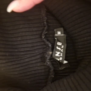 Svart ribbad klänning från Sense - Svart, tight ribbad klänning från Sense Woman i storlek M. Klänningen är ärmlös och har en kroppsnära passform med hög hals. Perfekt för dig som gillar en stilren och enkel look.