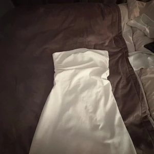 Vit axelbandslös långklänning - Snygg vit axelbandslös långklänning med figurnära passform. Klänningen har en stilren design och dragkedja baktill för enkel påklädning. 