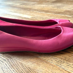 Rosa vintageskor från Vagabond - Snygga rosa ballerinaskor från Vagabond i mjukt skinn. Modellen har rund tå och öppen tå framtill för en cool touch. Platt sula gör dem bekväma att bära hela dagen. Perfekta för dig som vill sticka ut med färg på fötterna. Vintage 80-tsl.