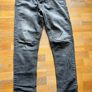 Replay grå jeans med raka ben - Säljer ett par grå jeans från Replay med snygg tvätt och klassiska fem fickor. Jeansen har raka ben och normal passform, med detaljerade sömmar på bakfickorna och Replay-märke i linningen. Perfekta för dig som gillar en stilren look.