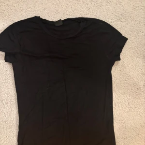 Svart basic t-shirt från Slazenger - Enkel svart t-shirt från Slazenger i klassisk modell med rund hals och korta ärmar. Tillverkad i mjuk bomull som är skön mot huden. Perfekt att matcha med jeans eller shorts för en clean och stilren look.