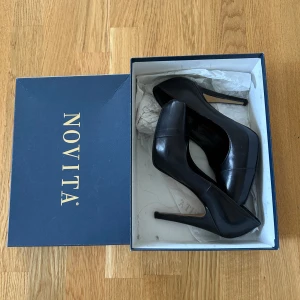 Svarta pumps från Novita i skinn - Klassiska svarta pumps från Novita i äkta skinn med spetsig tå och hög klack. Snygg och tidlös modell som passar perfekt till dig som vill ha en elegant look. Insidan har en diskret röd kant som ger en extra touch.
