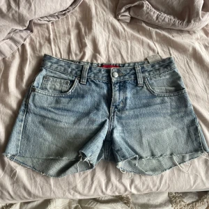 Ljusblå jeansshorts från Redstar - Snygga lågmidjade jeansshorts från Redstar med knappdetaljer på bakfickan. Midjemåttet är ca 37 cm när dom är liggandes.