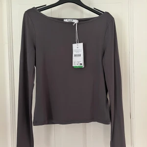 Grå long sleeve topp från NA-KD - Säljer en stilren mörkgrå långärmad topp från NA-KD med båtringad hals💗Toppen är i nytt skick, aldrig använd med prislapp kvar, är av superlent material och skulle passa perfekt till jeans eller en skjol nu till sommaren men även till en mysig outfit i höst💗säljer då den inte kommit till användning