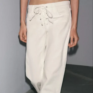 Vita jeans med medelhög midja. SLIM FIT - BOOTCUT- MODEL - Snygga vita jeans som sitter löst längs benen. Jeansen har även en cool snörning i midjan. Byxorna har raka bakfickor och är perfekta för en clean och trendig look. Jeansen är helt slutsålda på Zaras hemsida men man kan läsa mer om material och om jeansen på deras hemsida!! Jeansen är helt nya och aldrig använda med prislapp kvar!!