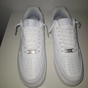 Nike Air Force 1 (pris diskuteras!) - Klassiska Nike Air Force 1 sneakers i helvitt skinn. Snygg och clean design med perforerad tå, rund tå och vit sula. Ikonisk Nike-logga på sidan och bak, samt metallbricka med 'AF1' på snörningen. Perfekta för dig som gillar klassiska skor som går med vilken outfit som helst!                                  Ha en trevlig dag!