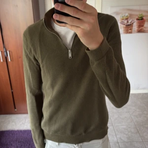 Olivgrön stickad half zip-tröja S - Säljer en olivgrön stickad tröja i storlek S med half zip-dragkedja vid halsen. Tröjan har långärmad passform och är tillverkad i ett grovt stickat material som ger en snygg och avslappnad look. Perfekt för lager-på-lager under kyliga dagar.