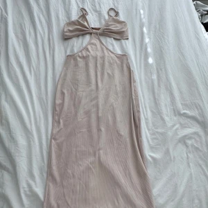 Beige ribbad långklänning cut out - Supersnygg beige långklänning med ribbad struktur och cut out-detalj vid bröstet. Klänningen har smala axelband och en figurnära passform upptill. Perfekt för dig som gillar minimalistisk och trendig stil.