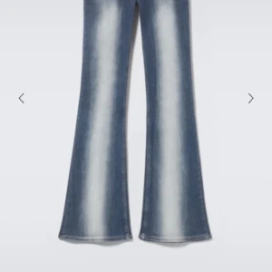 Blå bootcut jeans med slitningar - Snygga blå bootcut jeans med ljusa slitningar längs benen. Jeansen har klassisk femficksdesign och markerad utsvängning nertill för en retro vibe. Perfekta för dig som gillar en avslappnad men trendig look.