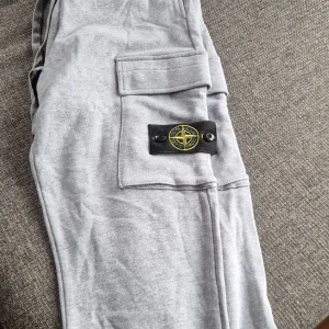 Grå mjukisbyxor från Stone Island - Sjukt sköna grå mjukisbyxor från Stone Island med klassiska loggan på benet. Byxorna har cargofickor på sidorna.