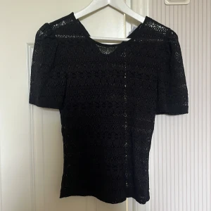 Svart spetsblus från Vila - Supersnygg svart blus från Vila i spets med puffärmar och rund halsringning. Blusen har ett detaljerat blommigt spetsmönster som ger en romantisk vibe och är lätt transparent. Perfekt att styla med jeans eller kjol för en trendig look.