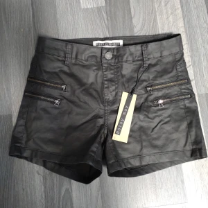 Nya Svarta shorts i skinnimitation med dragkedjor Noisy May - Snygga svarta shorts från Noisy May med coola dragkedjedetaljer framtill och klassiska bakfickor. Modellen är midwaist och har en stilren look som passar perfekt till sommaren. Storlek xs/s