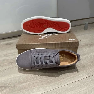 Grå sneakers från Louboutin st:43 - Snygga grå sneakers från Louboutin med klassisk röd sula och vit kant. Skorna har rund tå, snörning och är tillverkade i mocka med beige innersula. Perfekta för dig som vill ha en stilren och exklusiv look med en ikonisk touch.