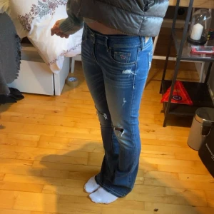 Bootcut jeans med en lågmidja - Snygga blå bootcut jeans med en lågmidja från Hollister med slitna detaljer och hål på knäna.