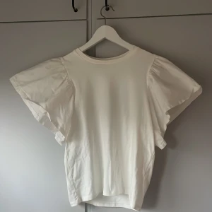 Vit blus med voluminösa ärmar Gina Tricot - Supersöt vit blus från Gina Tricot med voluminösa, korta ärmar som ger en trendig och luftig känsla. Rund halsringning och enkel, stilren design som passar perfekt till jeans eller kjol. Ärmarna är i skjortmaterial vilket gör toppen lite lyxigare. 💕💕