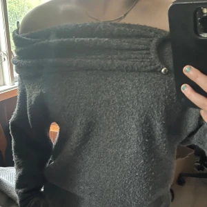 Mörkgrå offshoulder stickad tröja - Mysig mörkgrå stickad tröja med offshoulder-design och bred krage som dekoreras av två silvriga bollar framtill. Tröjan har lång ärm och en lite loose passform, perfekt för lager på lager under kyliga dagar, eller som en vanlig dag under hösten då det kanske regnar. Lite noppig men inget man tänker eftersom matrerialet på tröjan. Fick för två år sedan, använde den ibörjan men har tröttnat på den nu efter ett tag. Ordinarie pris 400 sek, säljs nu för 200kr mindre. Finns ej att köpa längre i butik