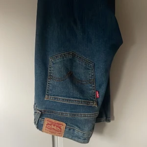 Levi's Superlow Bootcut jeans blå - Säljer ett par Levi's Superlow Bootcut jeans i klassisk blå tvätt. Jeansen har låg midja, bootcut-ben och snygga slitningar. Ikonisk Levi's-lapp bak och röda Levi's-tag på bakfickan. Superfina till en snygg blus eller kortare topp❣️längd: 30 midjemått: 27