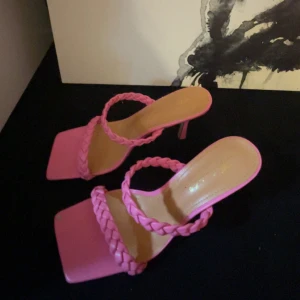 Rosa klackade sandaler med flätade band - Snygga rosa sandaler med hög klack och två flätade band över foten. Skorna har fyrkantig tå och en trendig design som verkligen sticker ut. Perfekta för dig som vill ha något extra till outfiten.