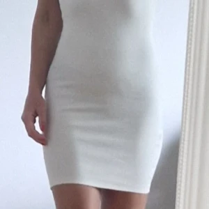 Vit ribbad ärmlös kortklänning - Säljer en vit, ribbad och tight kortklänning med ärmlös design och rundad hals. Klänningen har en clean och enkel look som sitter snyggt mot kroppen. Perfekt för dig som gillar minimalistisk stil och vill ha något som känns fräscht och modernt. Använd 1 gång så den är i ny skick.