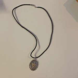 Svart halsband med vintage medaljong - Unikt svart halsband med oval medaljong i silverfärgad ram. Medaljongen har ett coolt motiv med ett ben i mitten och detaljer runt kanten. 