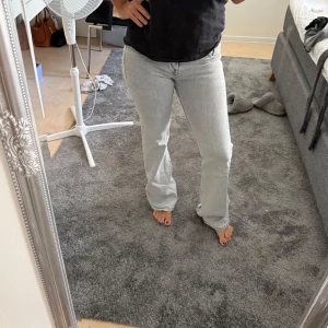 Ljusgråa, lågmidjade bootcut jeans - Säljer ett par ljusgrå jeans med bootcut passform och klassisk femficksdesign. Jeansen har normal midja och är tillverkade i ett mjukt bomullsmaterial med lite stretch. Perfekta för dig som gillar en avslappnad men ändå snygg look.