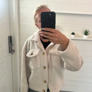 Vit teddyjacka från SHEIN XS - Säljer en fluffig vit teddyjacka från SHEIN i storlek XS. Jackan har två stora bröstfickor med lock, och en klassisk krage. Materialet är mjukt och teddy-liknande, perfekt för kyliga dagar. Jackan har lång ärm och en loose passform. Aldrig använd❤️