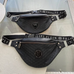 Svart magväska från Philipp Plein - Två svarta magväskor från Philipp Plein med präglat PP-mönster och coola emblem framtill. Väskorna har justerbara band med logotyp, dragkedja och detaljer i metall. Perfekt för att bära dina essentials med stil.