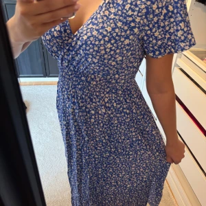 Blommig blå omlottklänning - Säljer en superfin blå klänning med vita blommor.